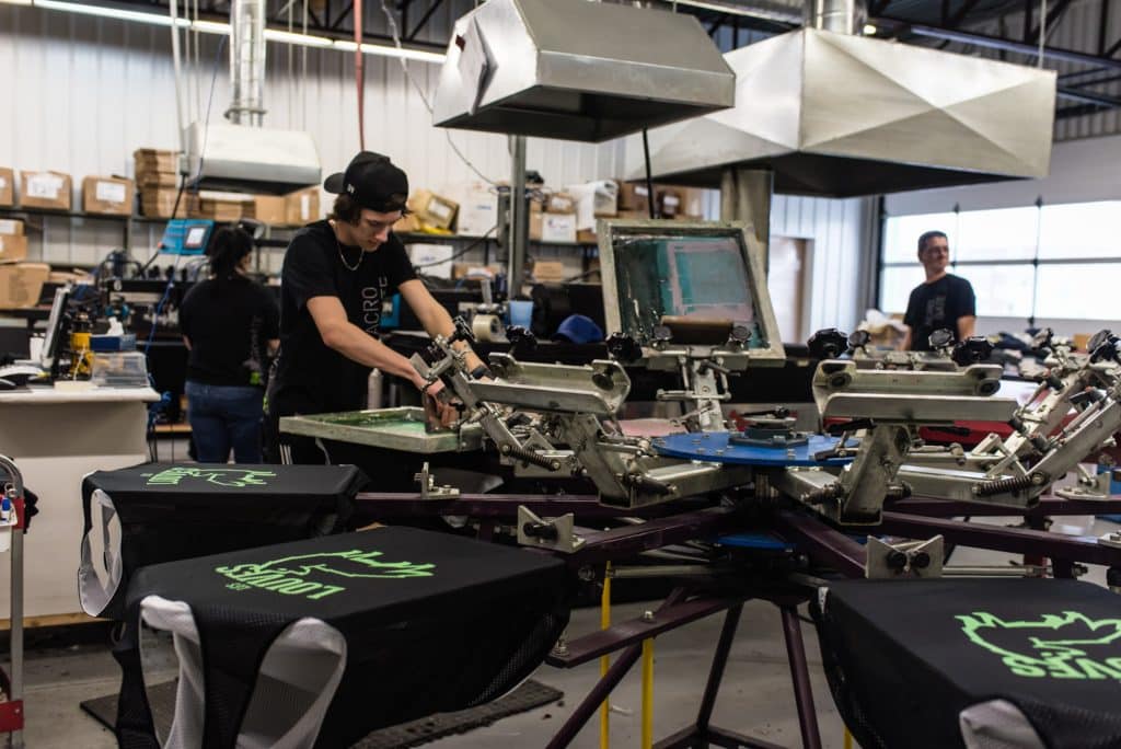 Atelier de sérigraphie d’Acrobate Promo: un employé imprime des maillots sur une presse rotative