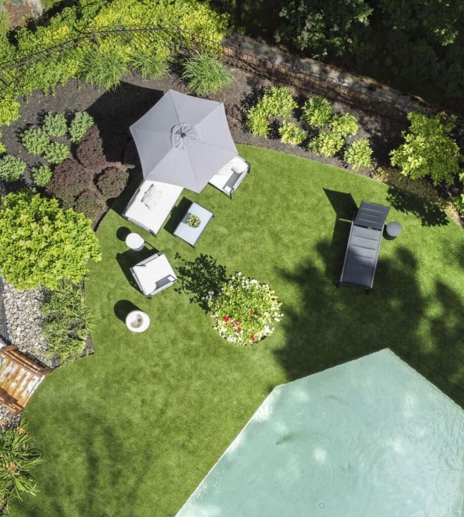 Vue aérienne d’une cour aménagée: pelouse, plates-bandes, mobilier de jardin et piscine